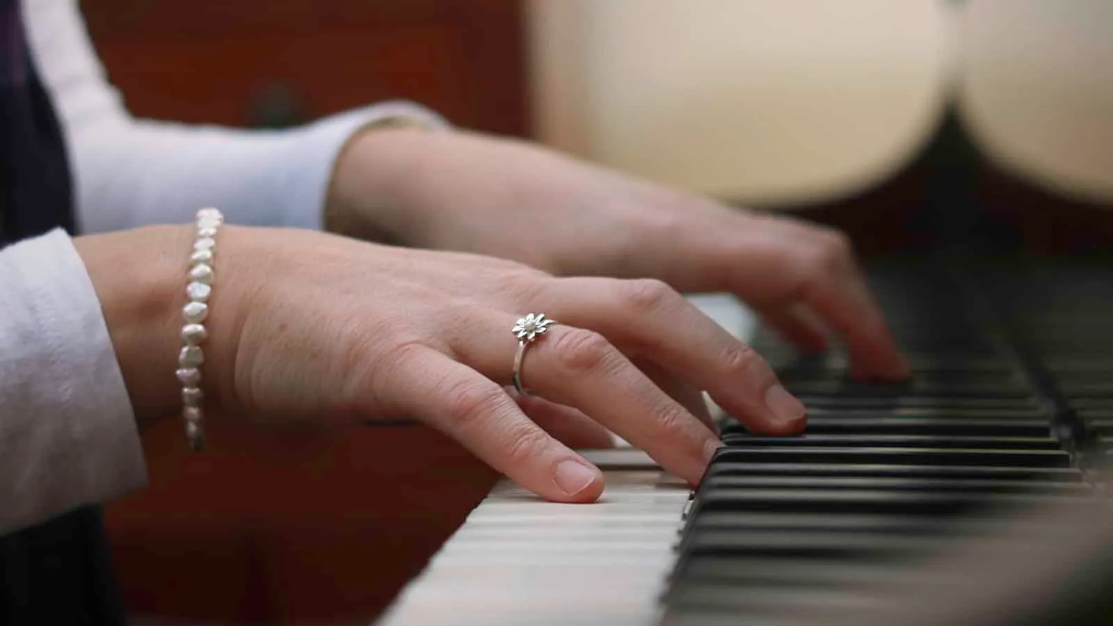 A hand playing the piano, with a ring and a pearl bracelet